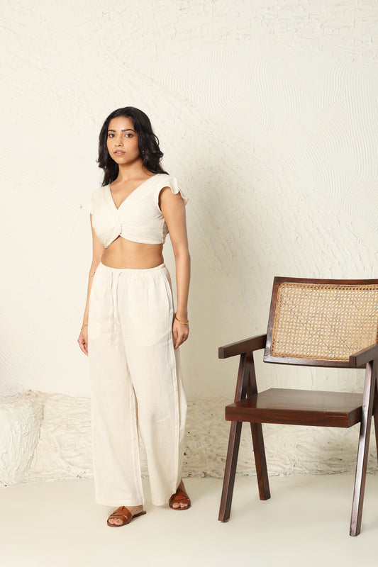Woman in a white outfit standing next to a wooden chair with wicker backrest against a light-colored wall.