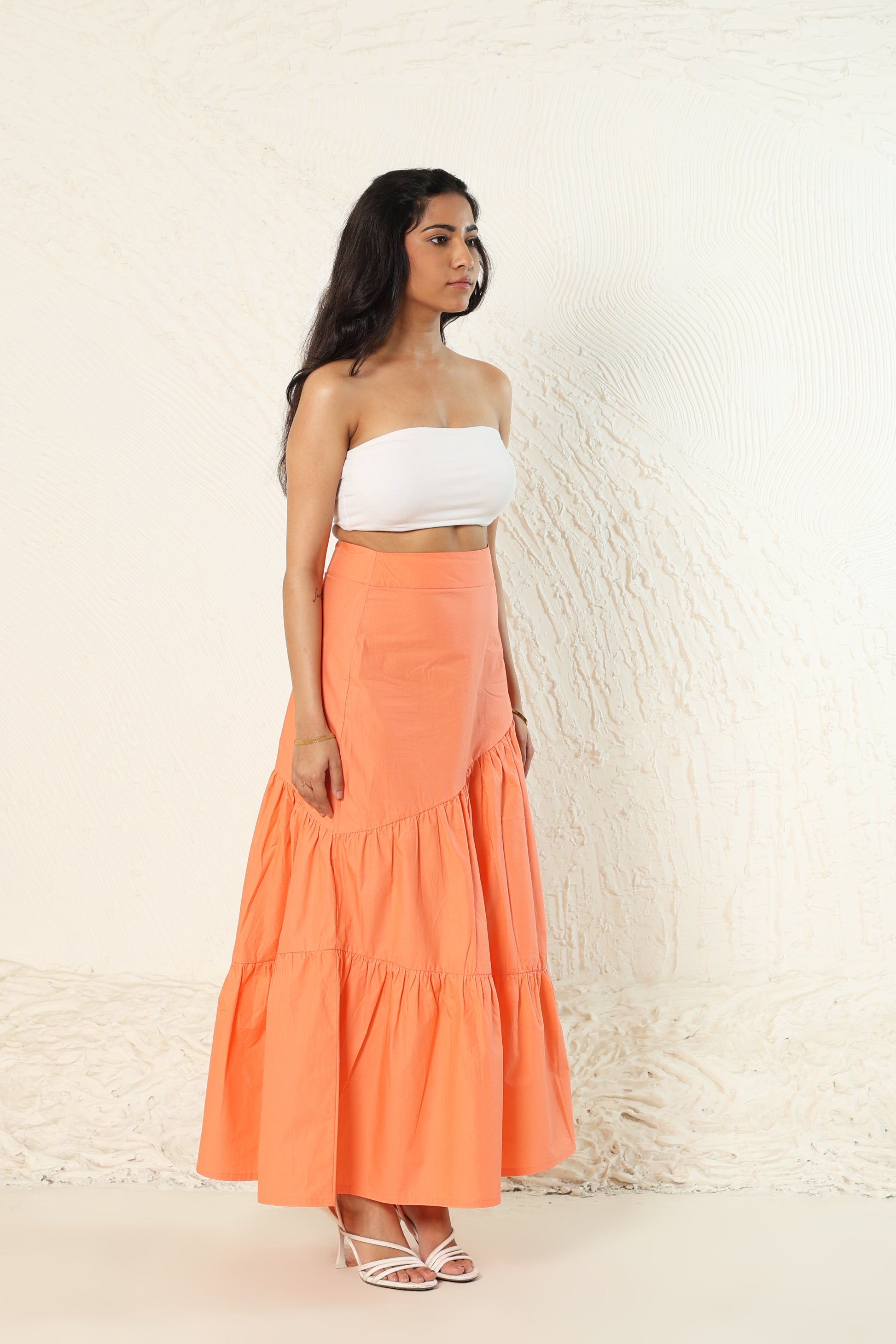 Woman wearing a white top and orange skirt against a light background