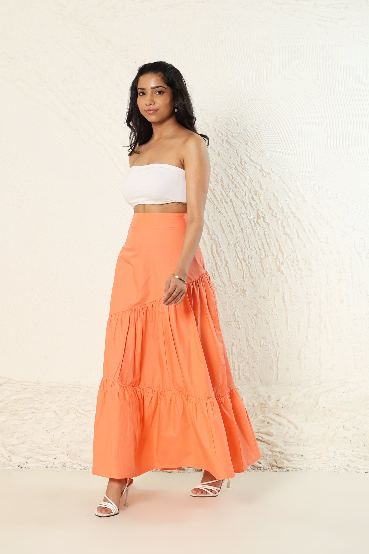 Woman wearing a white top and orange skirt against a white brick wall.