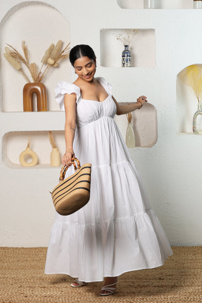 Woman in a white dress holding a straw bag in a room with shelves and decor.