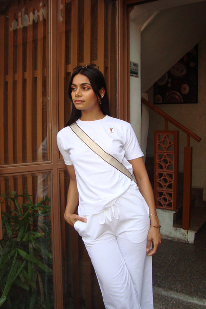 Woman in a white outfit with a beige bag standing indoors.