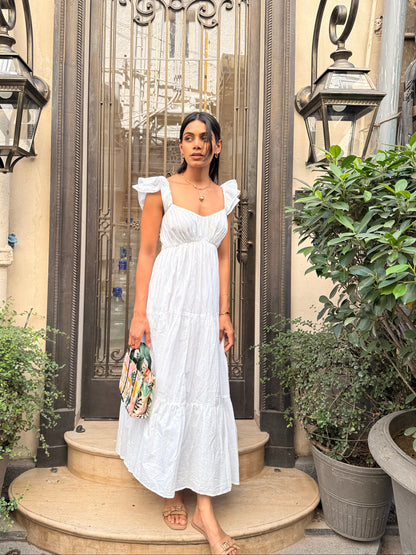 Woman in a white dress standing in front of a decorative door with plants around.