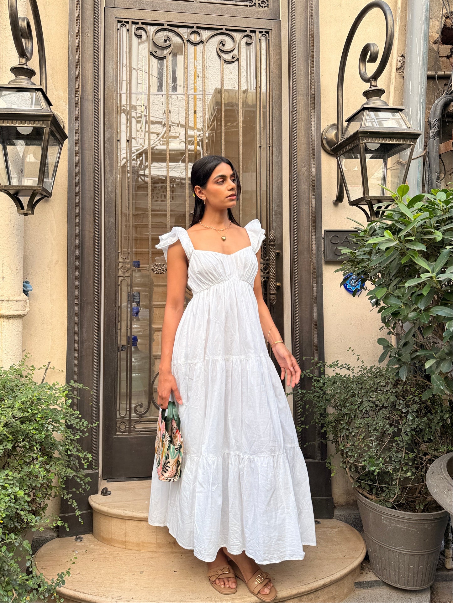 Woman in a white dress standing in front of a decorative metal gate.