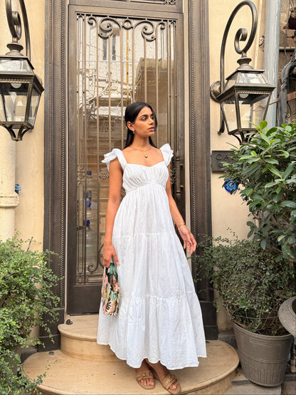 Woman in a white dress standing in front of a decorative metal gate.