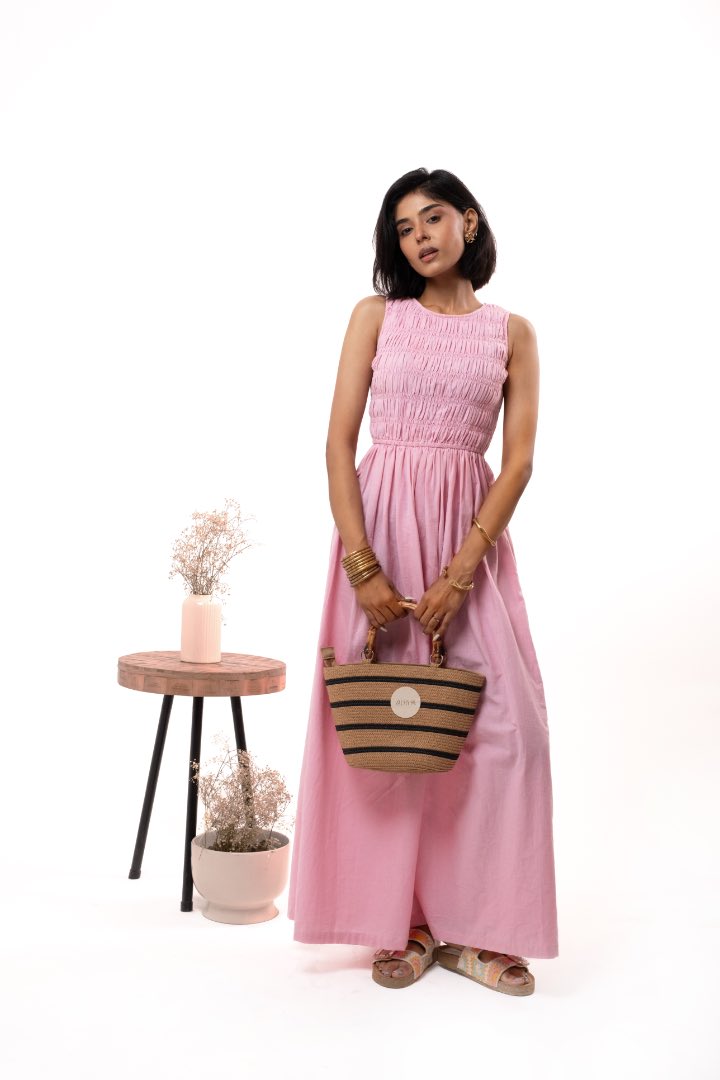 Woman in a pink dress holding a basket, standing next to a small table with plants on a white background