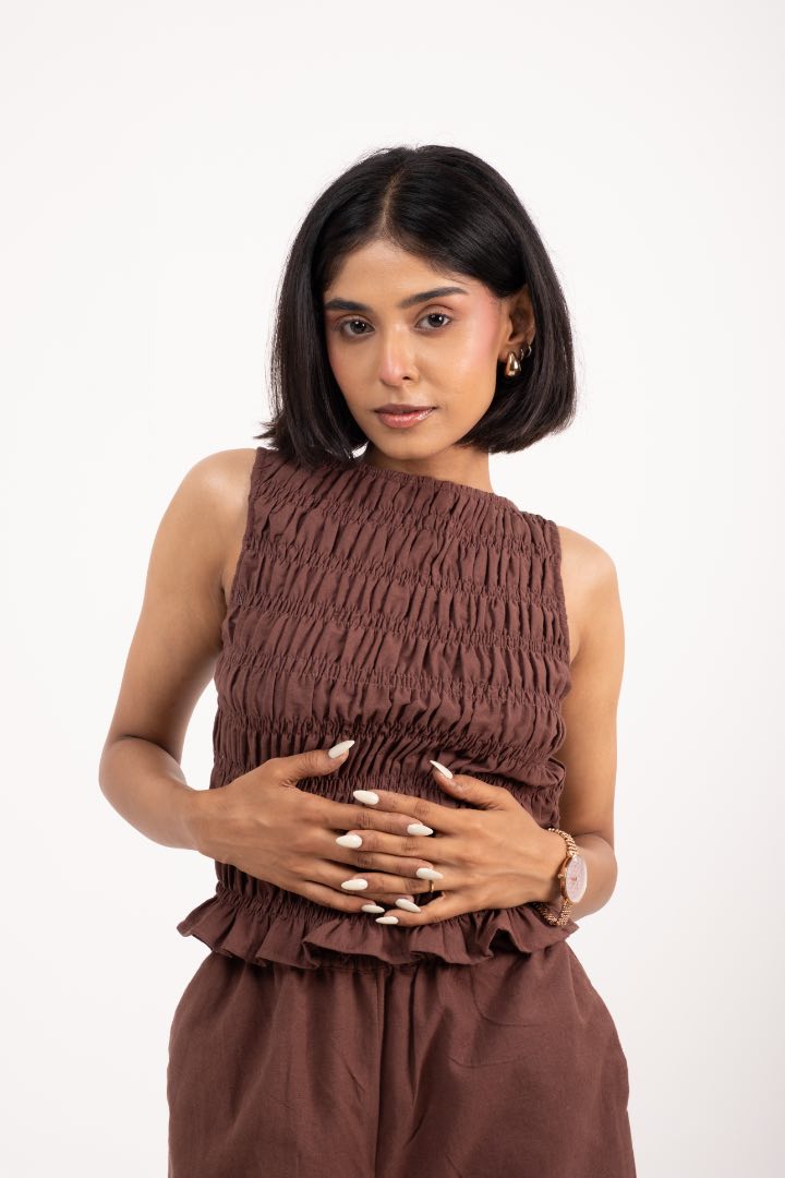 Woman wearing a brown sleeveless top and pants on a white background