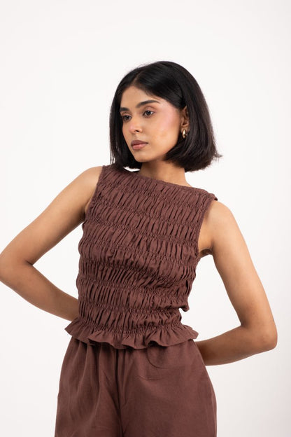 Woman wearing a brown sleeveless top and pants on a white background