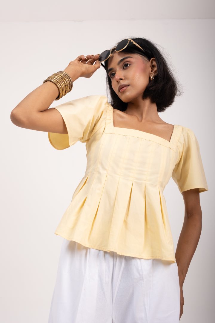 Woman wearing a light yellow top and white pants against a plain background