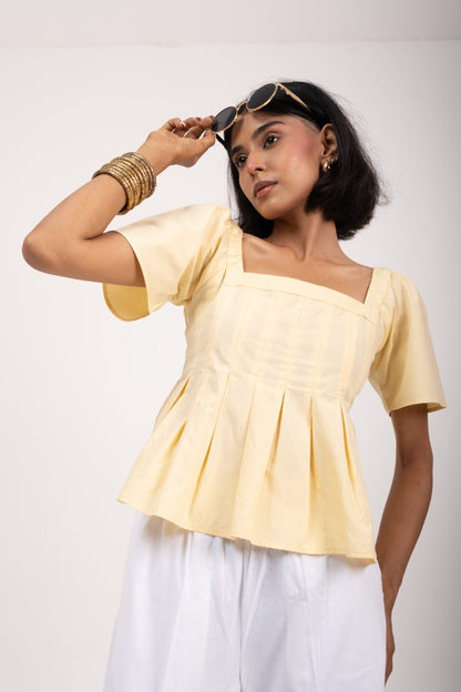 Woman wearing a light yellow top and white pants against a plain background